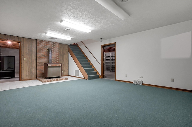 finished below grade area featuring a wood stove, carpet flooring, stairs, wooden walls, and baseboards