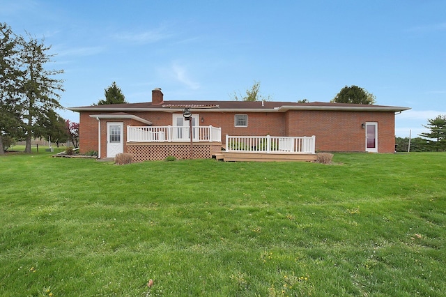 back of house with a yard, brick siding, a wooden deck, and a chimney