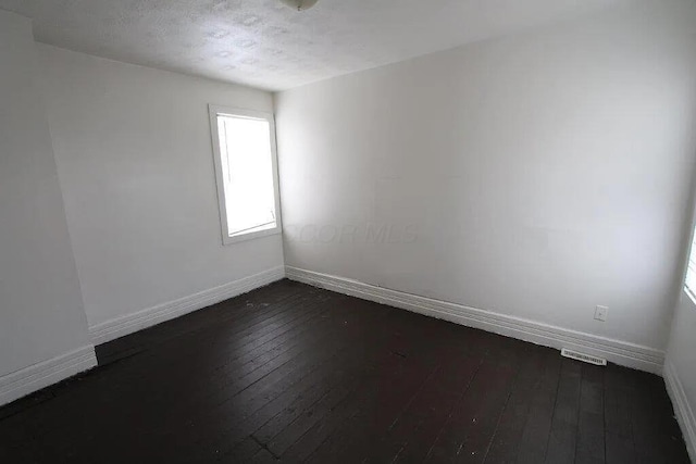 unfurnished room featuring visible vents, baseboards, and dark wood finished floors