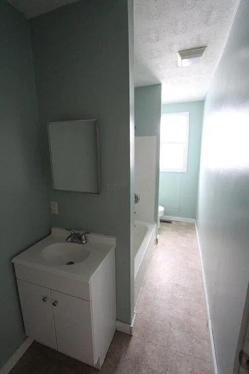 bathroom featuring vanity, a textured ceiling, toilet, a washtub, and visible vents