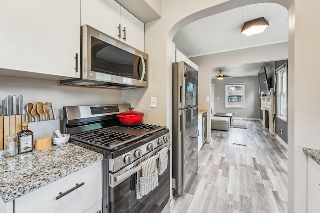 1329 Studer Ave, Columbus, OH 43206 - kitchen with stainless steel appliances, a ceiling fan, light wood-style floors, white cabinets, and arched walkways