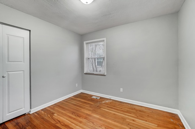 unfurnished room with a textured ceiling, visible vents, wood finished floors, and baseboards