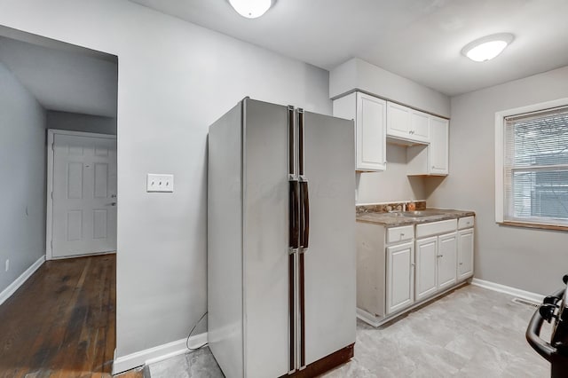 kitchen with white cabinetry, baseboards, a sink, and freestanding refrigerator