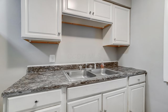 kitchen featuring dark countertops, a sink, and white cabinetry