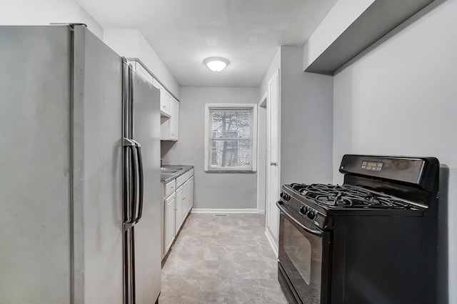 kitchen featuring black gas stove, white cabinets, freestanding refrigerator, and baseboards