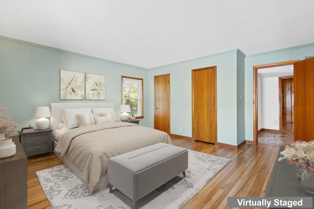 bedroom featuring light wood-type flooring, ornamental molding, baseboards, and two closets
