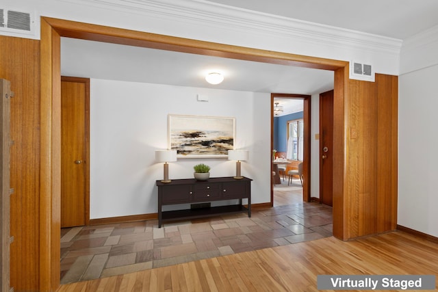 corridor with crown molding, baseboards, wood finished floors, and visible vents