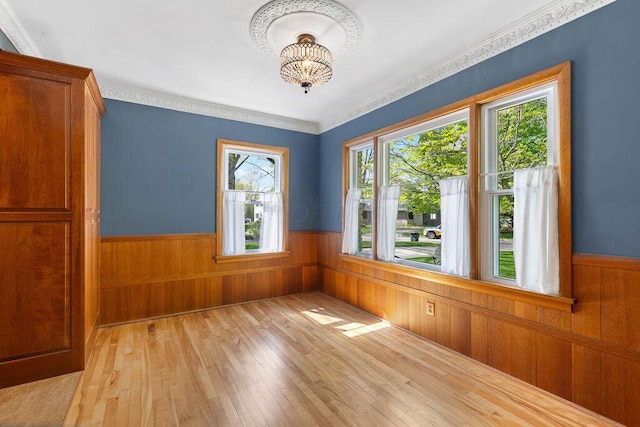 unfurnished room with ornamental molding, light wood-style floors, wooden walls, a wainscoted wall, and a notable chandelier
