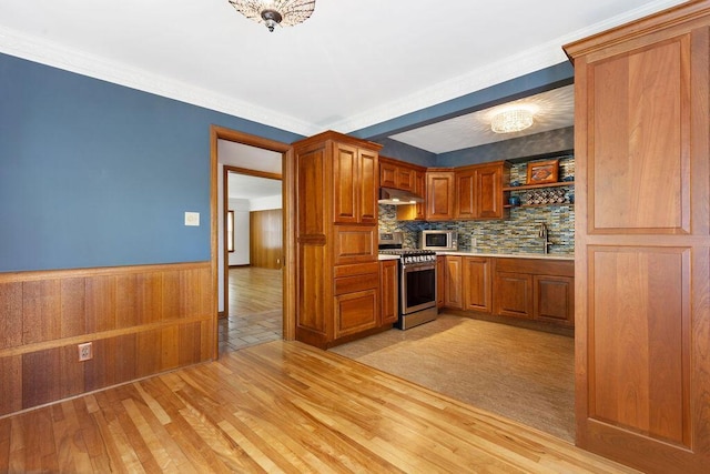 kitchen with light wood-type flooring, light countertops, under cabinet range hood, brown cabinets, and stainless steel appliances