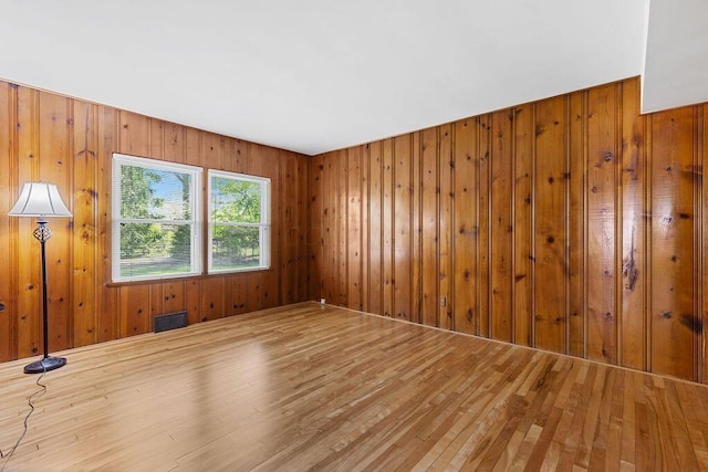 unfurnished room with visible vents, wood finished floors, and wooden walls