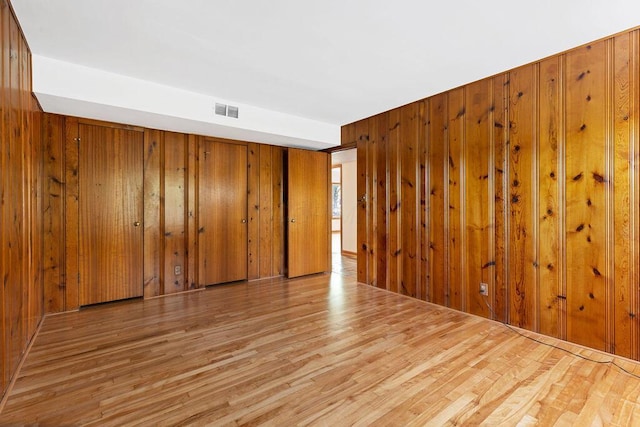 unfurnished room with wooden walls, visible vents, and wood finished floors