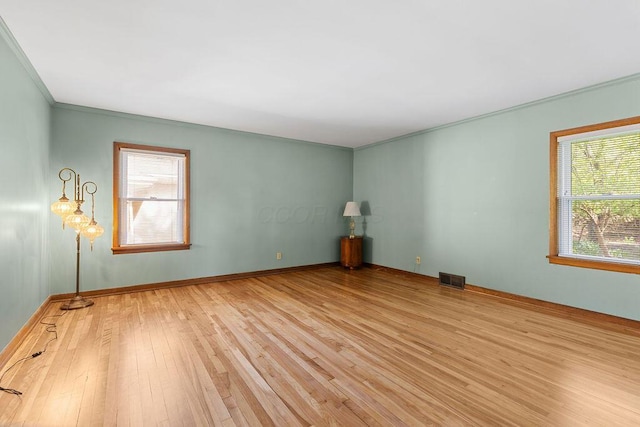 empty room featuring visible vents, plenty of natural light, ornamental molding, and hardwood / wood-style floors