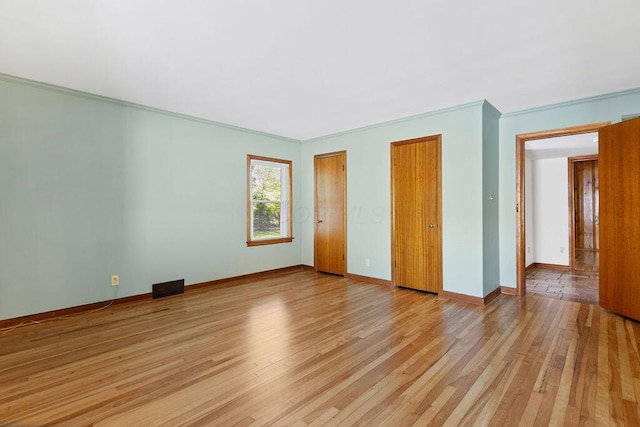 unfurnished bedroom featuring multiple closets, baseboards, ornamental molding, and light wood finished floors