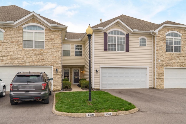 multi unit property featuring a garage, stone siding, and a shingled roof