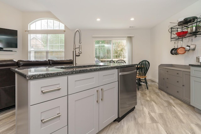 kitchen featuring dark stone countertops, a healthy amount of sunlight, dishwasher, and a sink