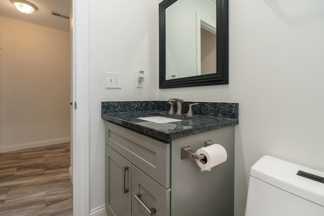 half bath featuring vanity, baseboards, toilet, visible vents, and wood finished floors