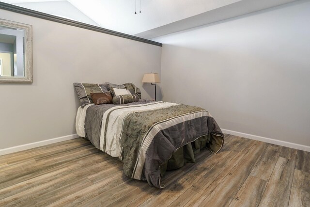 bedroom with baseboards, vaulted ceiling, and wood finished floors