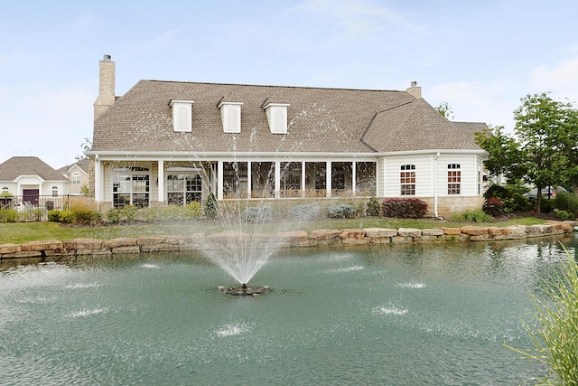 rear view of house with a water view, fence, a chimney, and a shingled roof