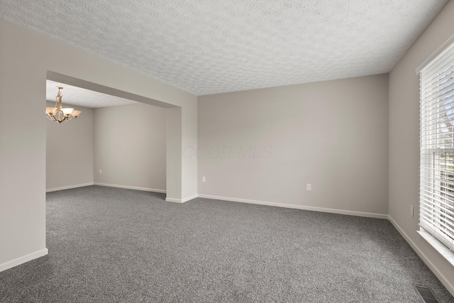 empty room featuring dark colored carpet, a notable chandelier, a textured ceiling, and visible vents