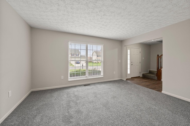 carpeted spare room featuring stairs, visible vents, baseboards, and a textured ceiling