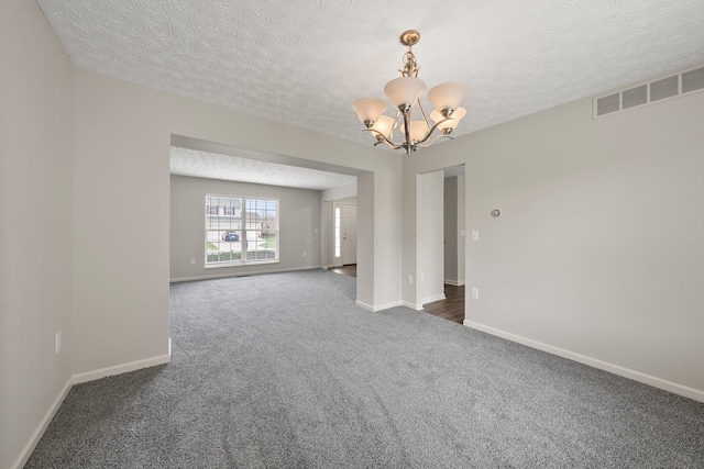 unfurnished room with dark colored carpet, baseboards, an inviting chandelier, a textured ceiling, and visible vents