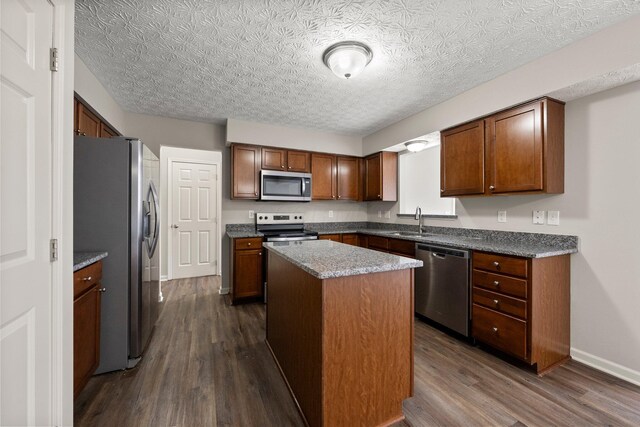 kitchen with dark wood-style flooring, baseboards, a kitchen island, appliances with stainless steel finishes, and a sink