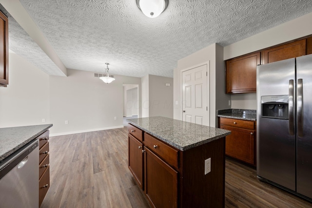 kitchen featuring dark wood-style flooring, a kitchen island, dark stone countertops, and stainless steel appliances