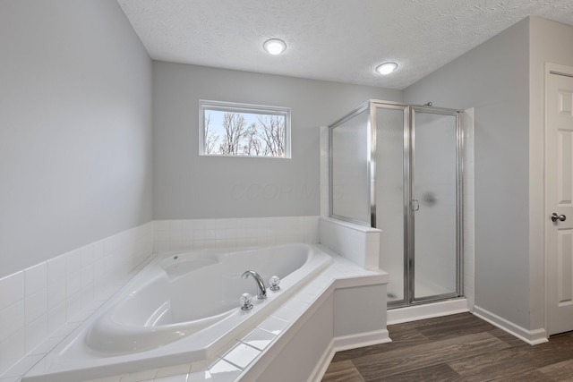 bathroom featuring a bath, a textured ceiling, wood finished floors, a stall shower, and baseboards