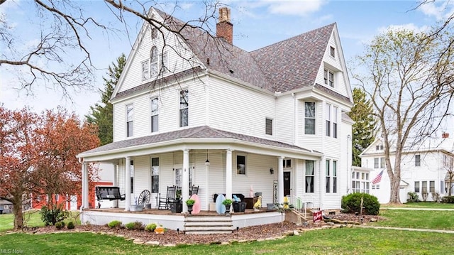 victorian-style house featuring roof with shingles, a porch, a front lawn, and a chimney