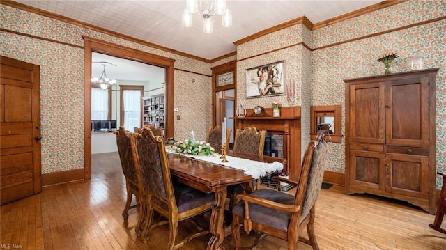 dining room featuring crown molding, light wood-type flooring, a notable chandelier, and wallpapered walls