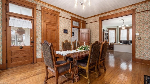 dining space with an inviting chandelier, light wood-style flooring, and wallpapered walls