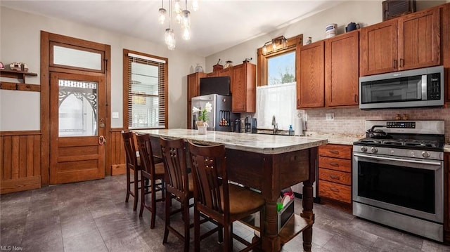 kitchen featuring tasteful backsplash, a center island, appliances with stainless steel finishes, brown cabinetry, and wainscoting