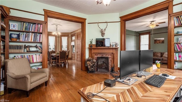 interior space featuring a fireplace, wood-type flooring, and ceiling fan with notable chandelier