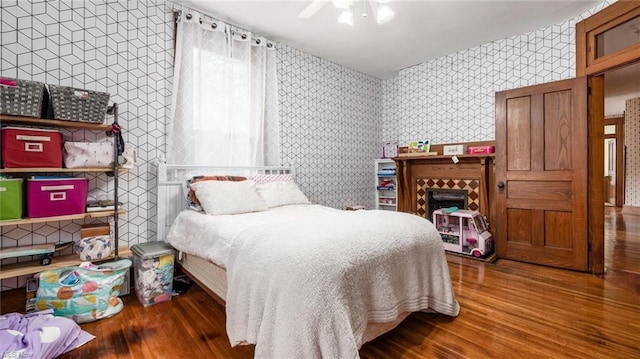 bedroom with ceiling fan, wallpapered walls, and wood finished floors