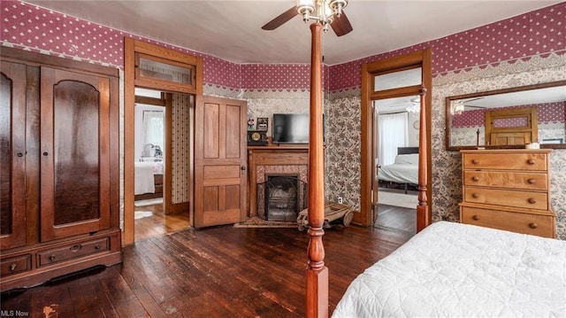 bedroom featuring wallpapered walls, dark wood-style floors, and a fireplace with raised hearth