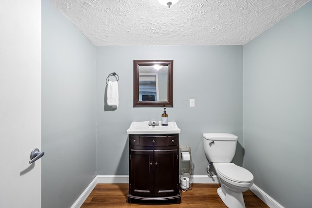 bathroom featuring a textured ceiling, toilet, baseboards, wood finished floors, and vanity