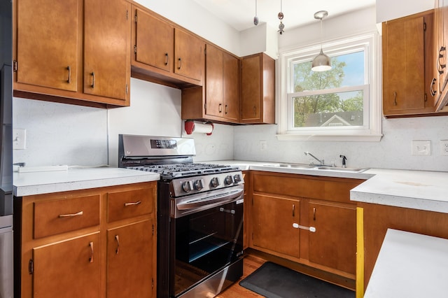 kitchen with stainless steel range with gas stovetop, a sink, brown cabinets, and light countertops
