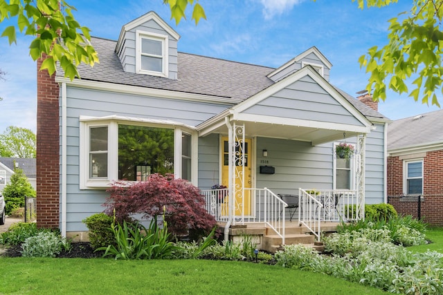 view of front of property featuring covered porch, a front lawn, and roof with shingles