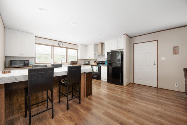 kitchen featuring light wood-style floors, a kitchen bar, wall chimney exhaust hood, white cabinetry, and black appliances