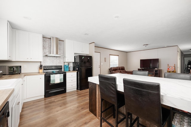 kitchen featuring light countertops, white cabinets, black appliances, light wood-style floors, and wall chimney exhaust hood