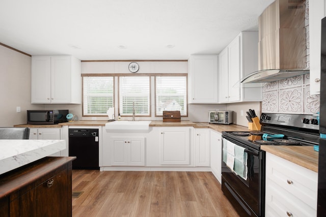 kitchen featuring white cabinetry, a sink, black appliances, light wood-style floors, and wall chimney exhaust hood