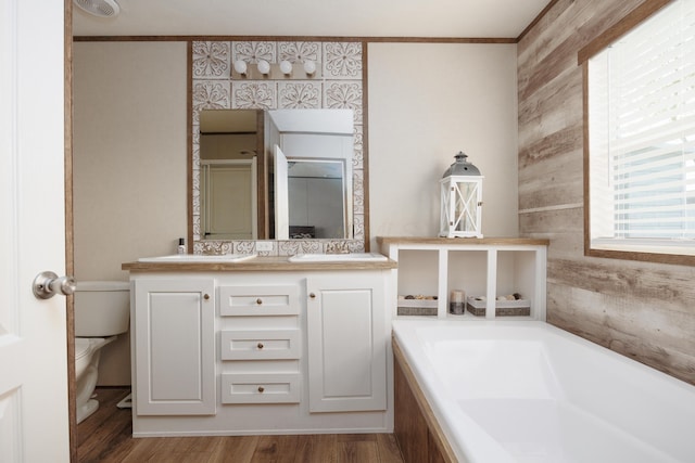 bathroom with double vanity, a bath, wood finished floors, a sink, and toilet