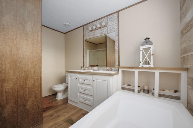 bathroom featuring crown molding, a shower with door, wood finished floors, toilet, and a sink