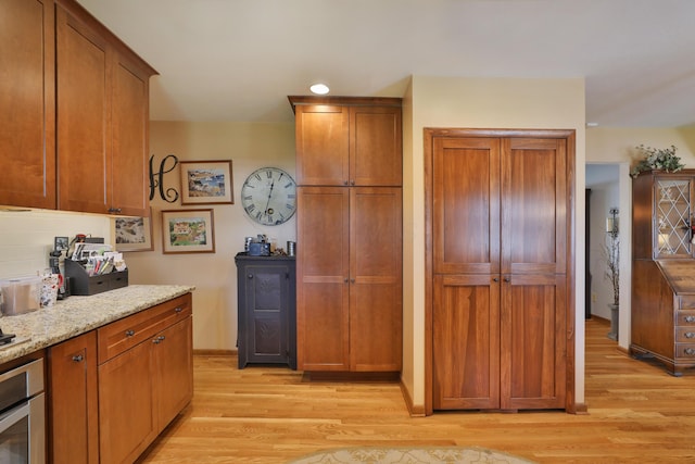 5580 Millington Rd, Columbus, OH 43235 - kitchen featuring oven, brown cabinets, light wood finished floors, and light stone counters