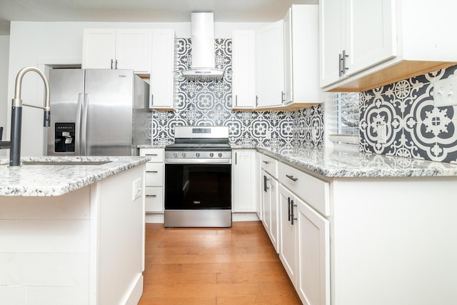 kitchen with light wood-style floors, wall chimney exhaust hood, appliances with stainless steel finishes, and white cabinetry