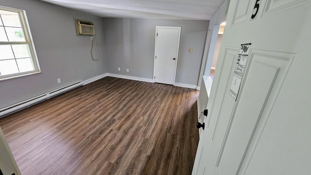 empty room with dark wood-type flooring, a baseboard radiator, baseboards, and an AC wall unit