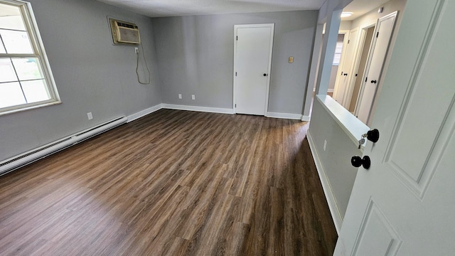 spare room with dark wood-type flooring, baseboard heating, baseboards, and a wall unit AC