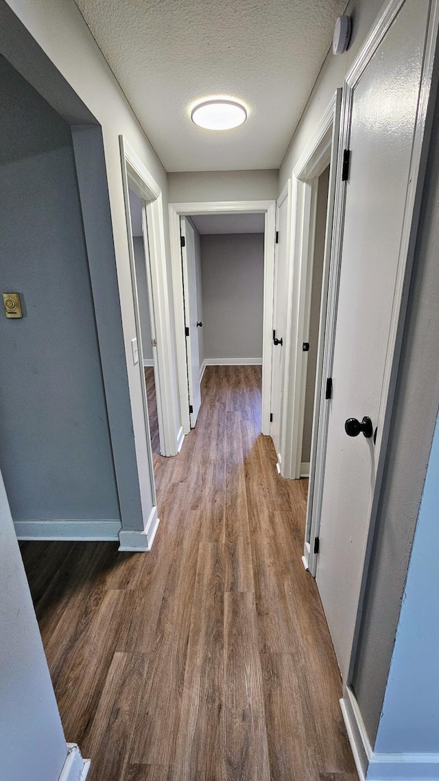 hall featuring baseboards, wood finished floors, and a textured ceiling