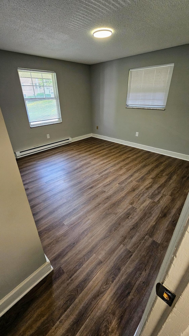 empty room with dark wood-type flooring, baseboards, a textured ceiling, and baseboard heating