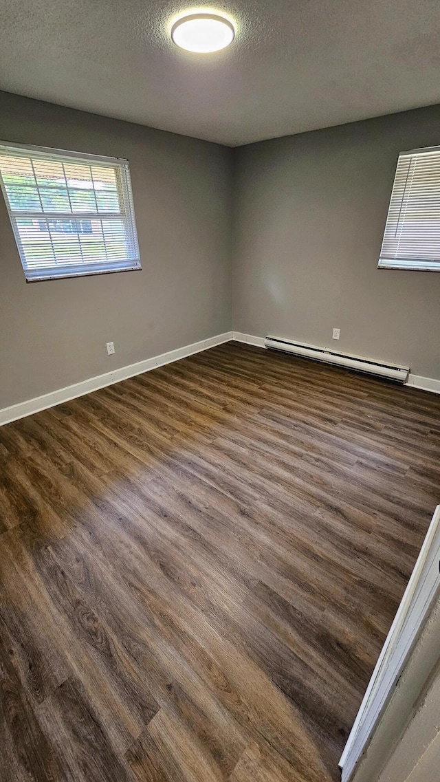 empty room featuring baseboard heating, a textured ceiling, baseboards, and dark wood finished floors